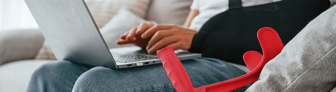 person mit gipsarm und krücke am laptop