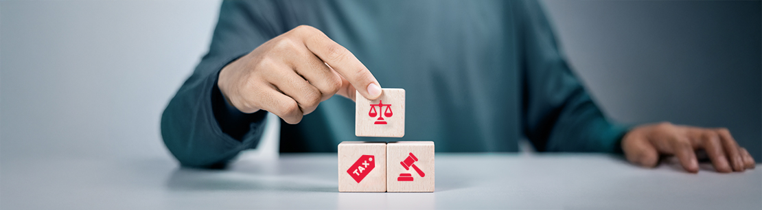 Eine Hand, die Holzklötze mit Symbolen stapelt. Die Symbole stehen für Steuer (Tax), Legal (Richterhammer) und Gerechtigkeit (Waage).
